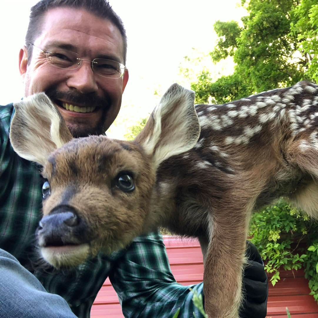 smiling man crouching next to a baby Reindeer